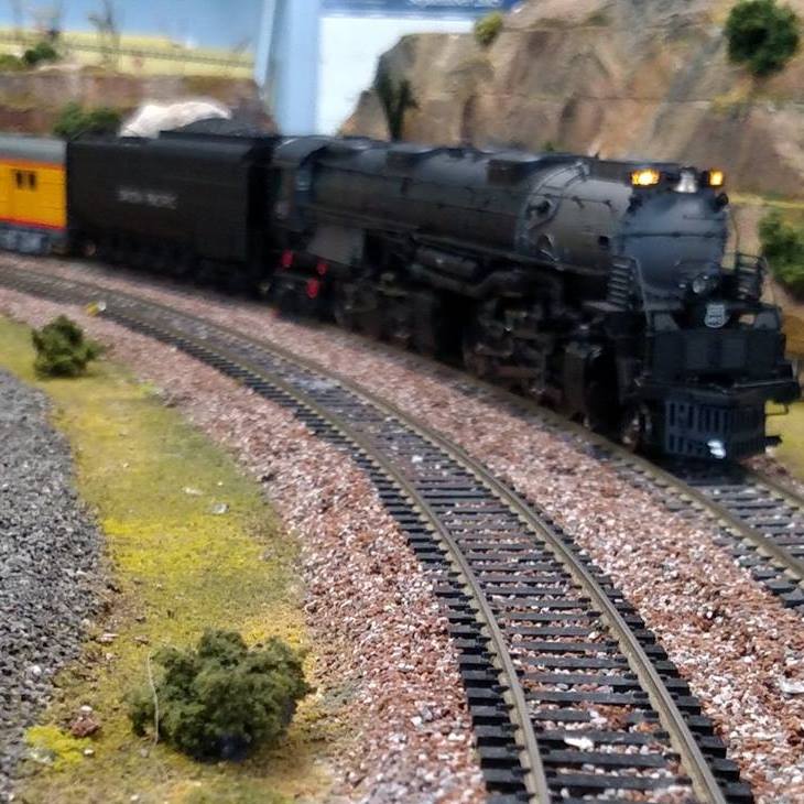 Detailed HO-scale steam locomotive rounding a curve on realistic track with scenery