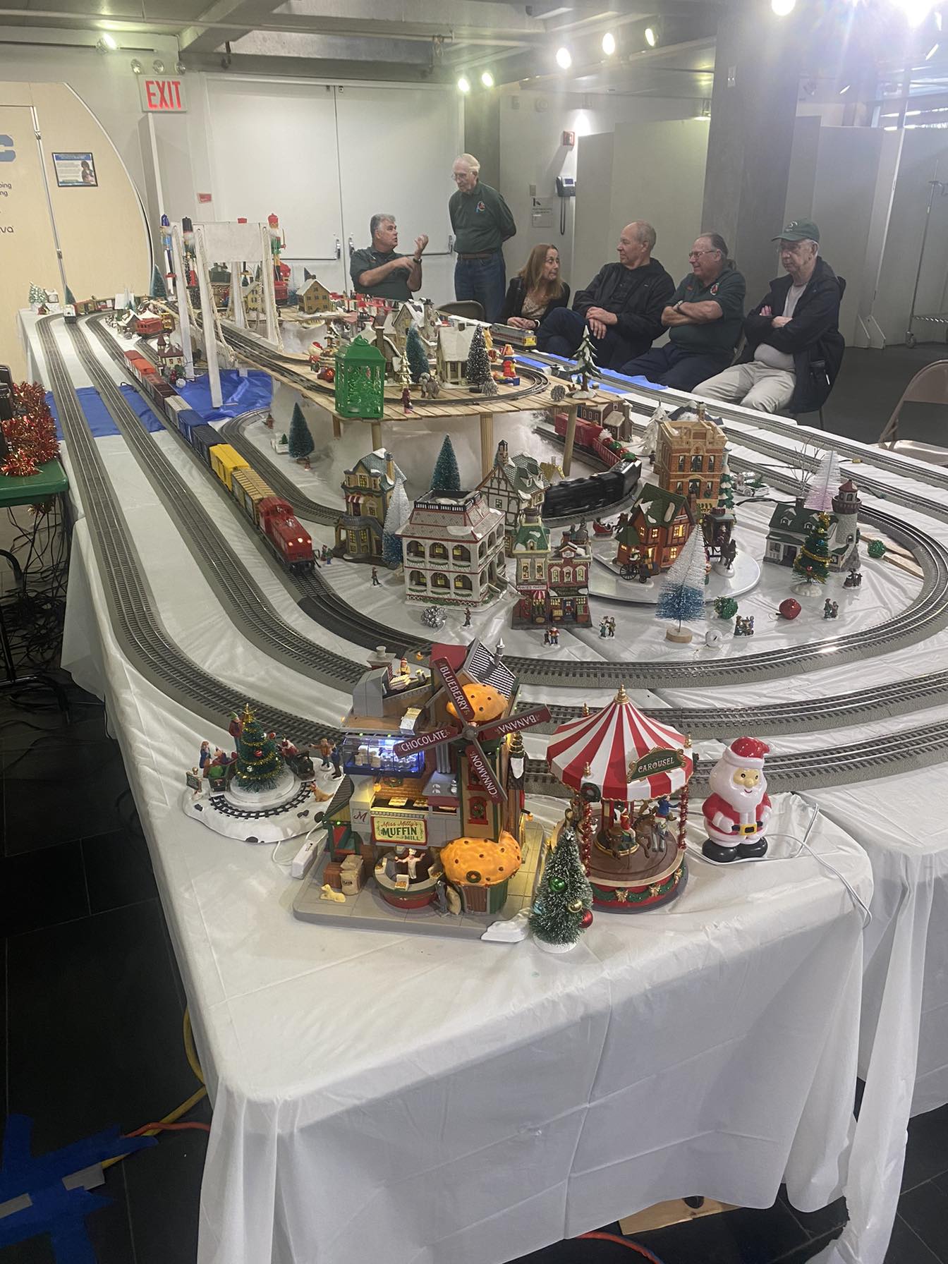 Holiday Train Show with elaborate Christmas village layout, multiple running trains, and club members